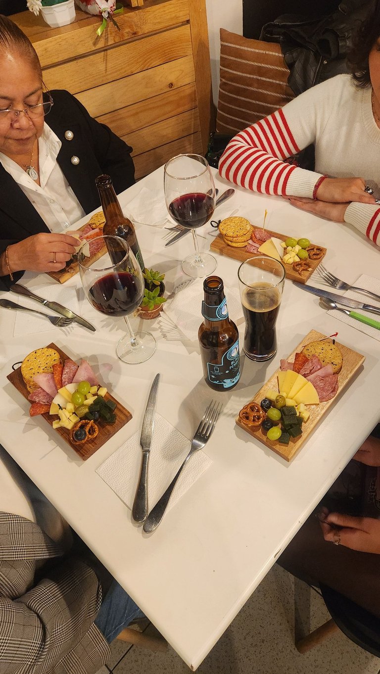 Friends enjoy individual charcuterie boards with wine and craft beer at a restaurant table.