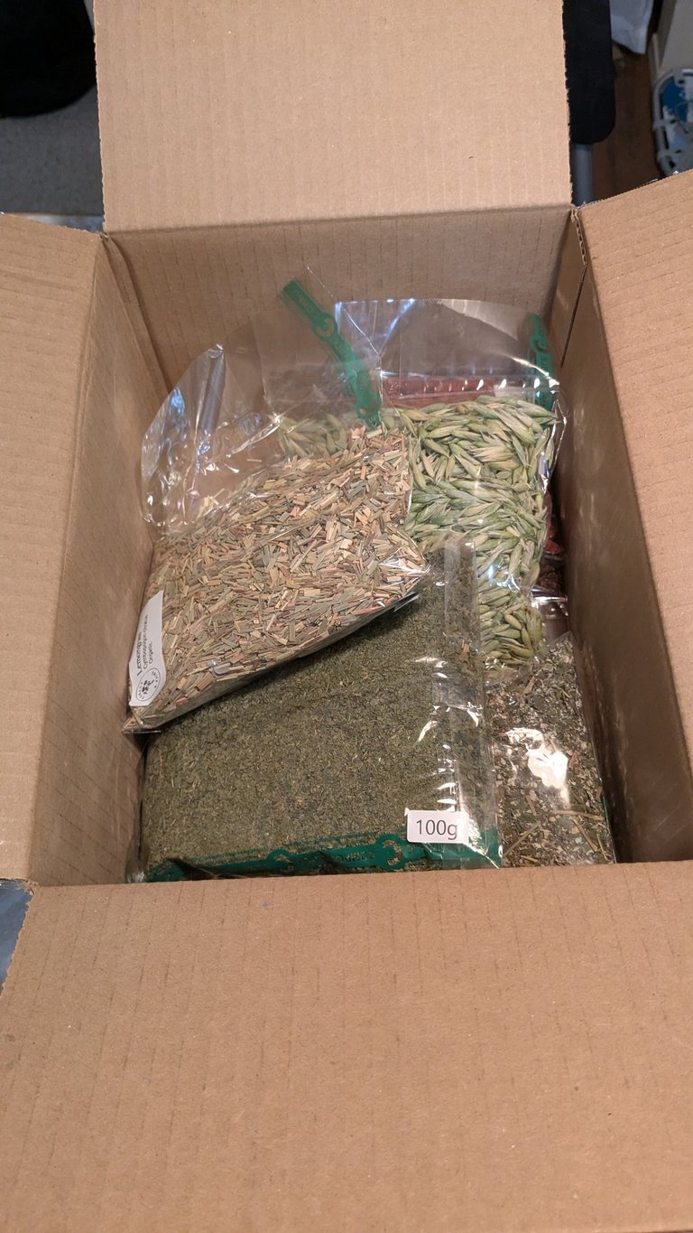 Open cardboard box containing several plastic bags filled with dried herbs and tea ingredients.