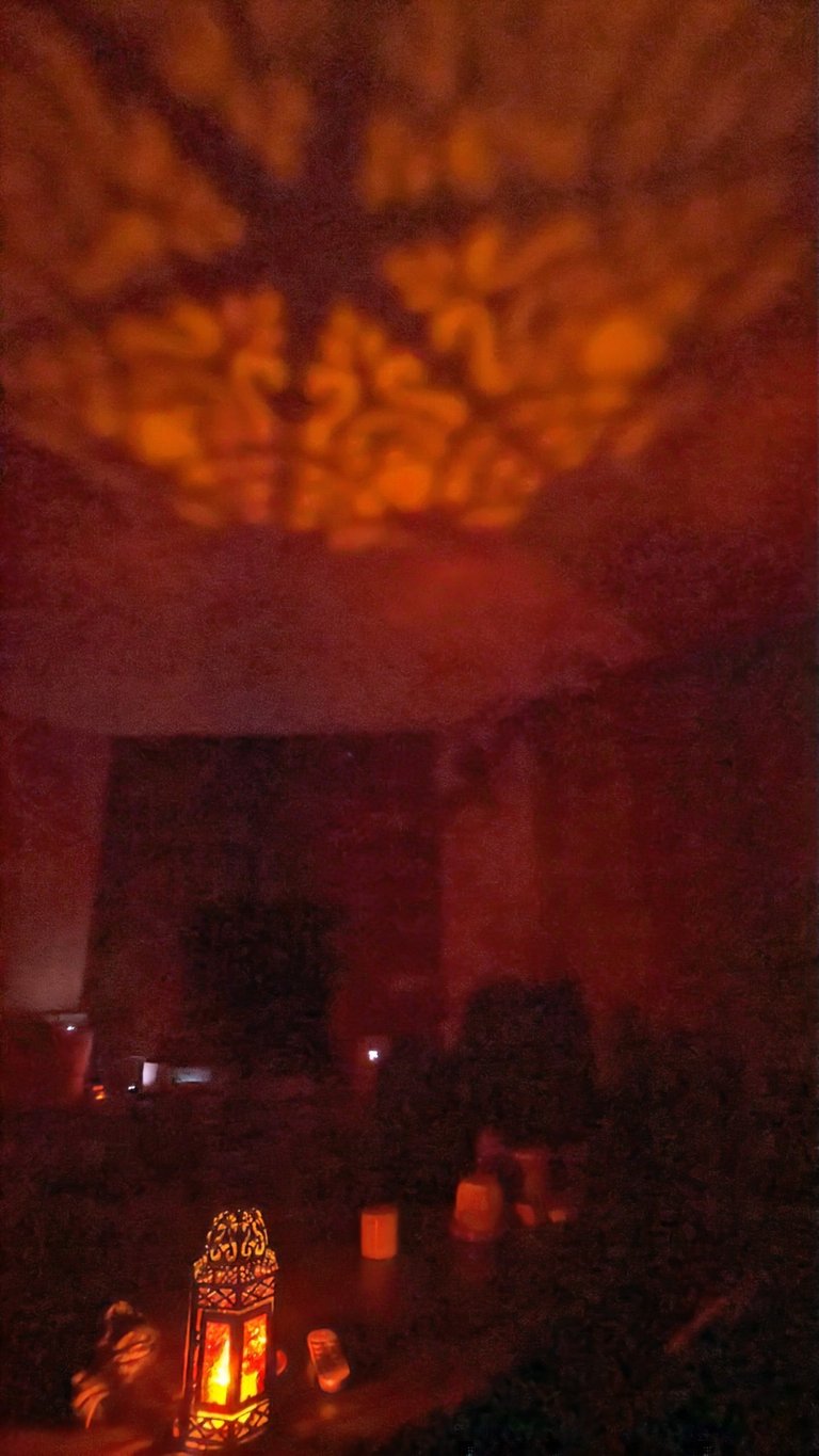 Lit candle lantern casting patterned light onto a wall in a dark room.