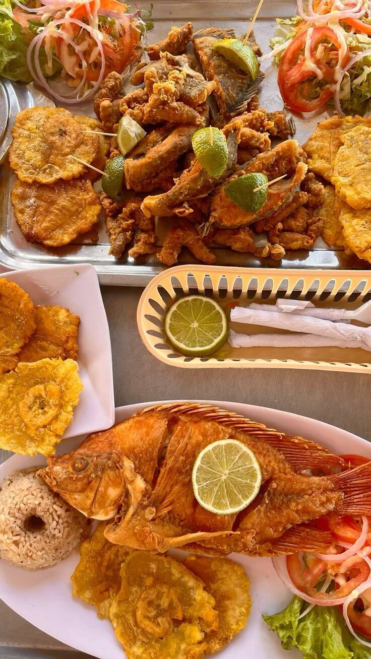 Crispy fried whole tilapia served with golden tostones, rice, and fresh salad garnish.