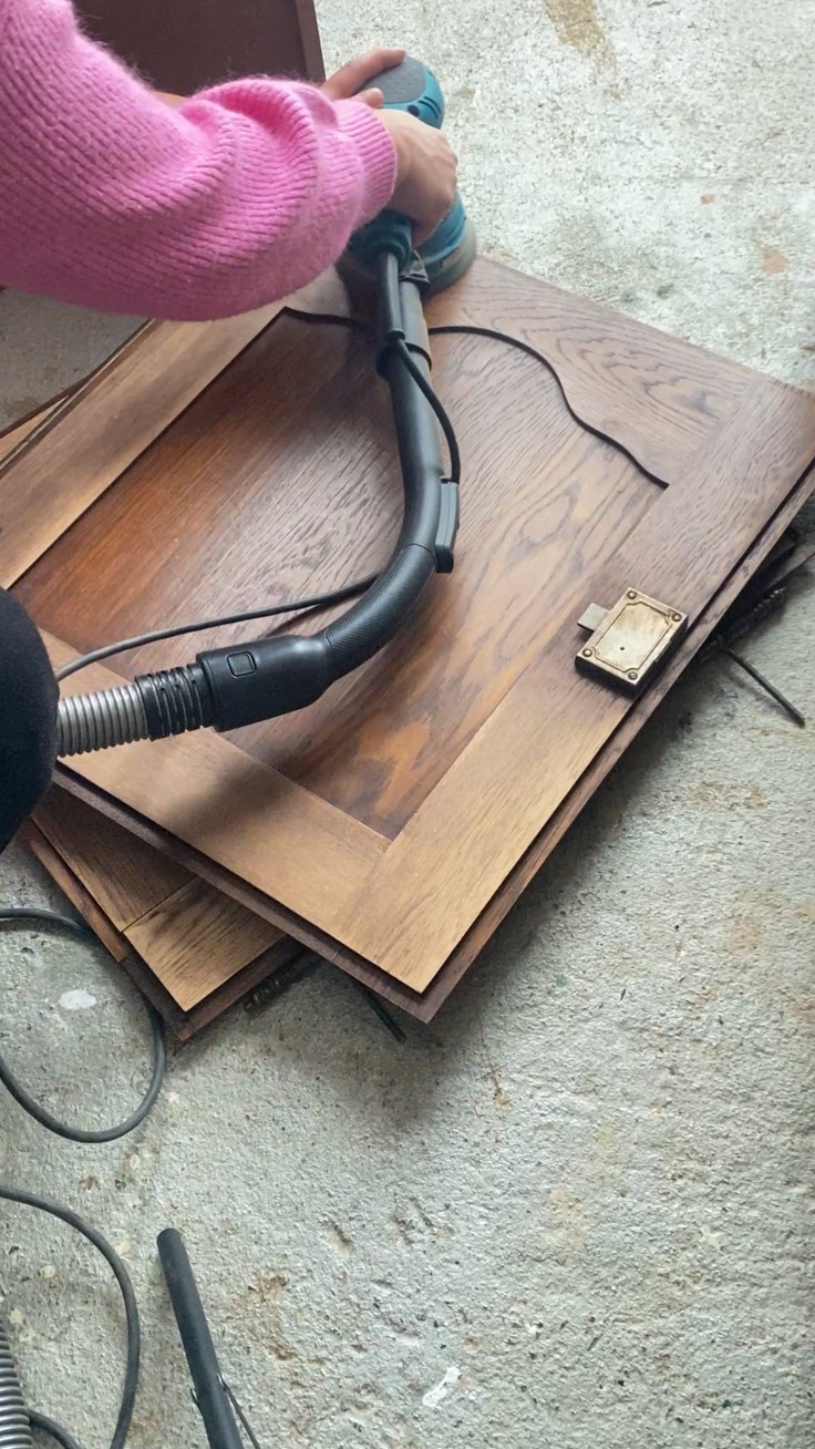 Cendrine l'artisane ponce une porte de meuble ancien pour le rénover dans l'atelier Chêne & Chiné