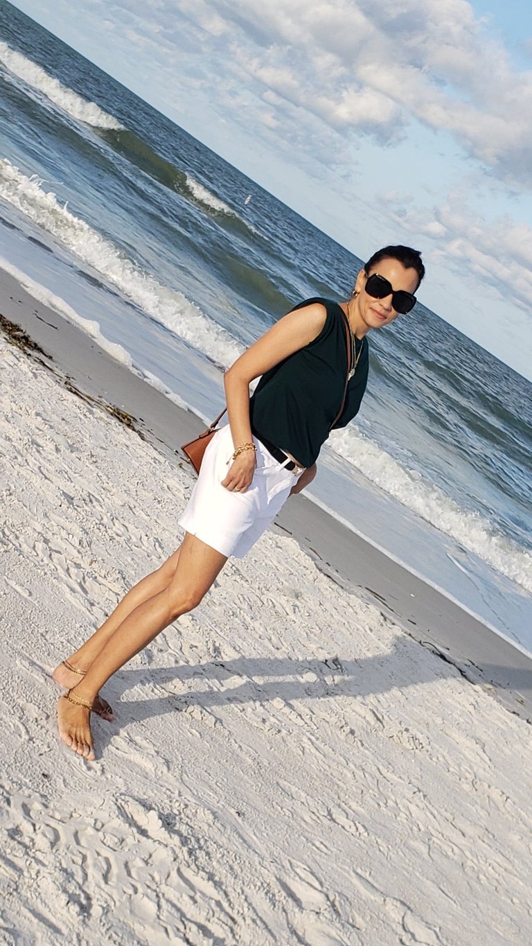 a woman in white shorts and sunglasses on a beach