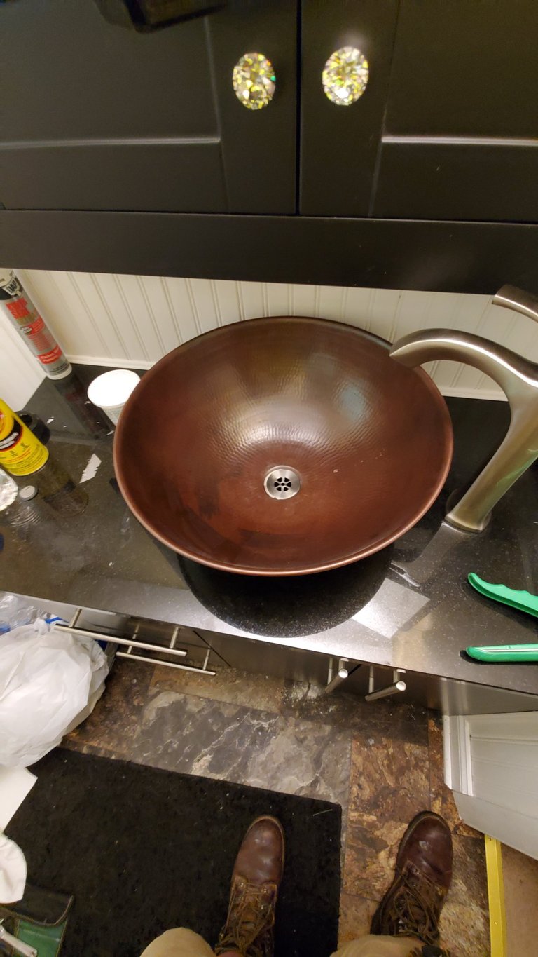 Hammered copper vessel sink installed on a black granite countertop with a brushed nickel faucet.