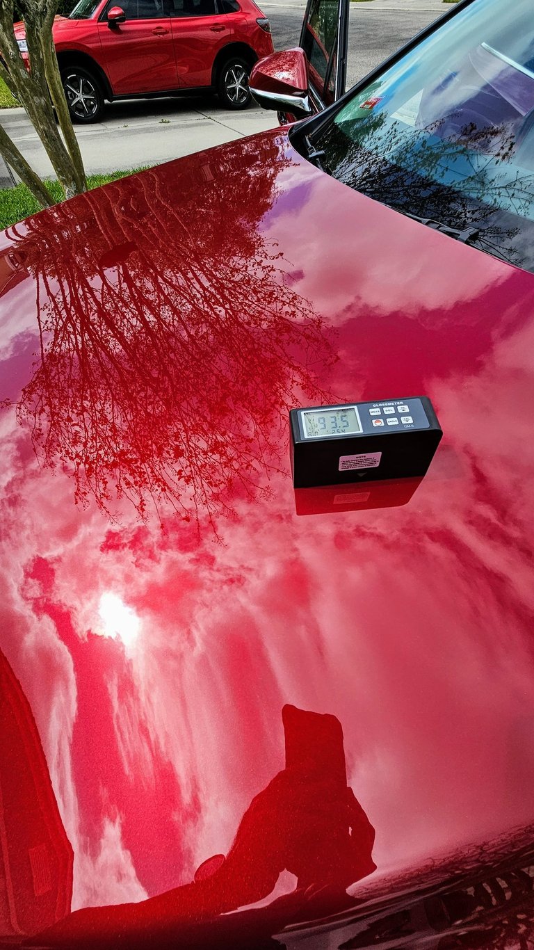 a ceramic coated red car with a gloss meter measuring the gloss factor on the hood of a red car