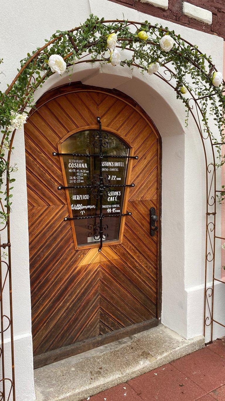 Rustic wooden door of the Cosiana Restaurant and Istons Hotel, framed by a flowering rose arch.
