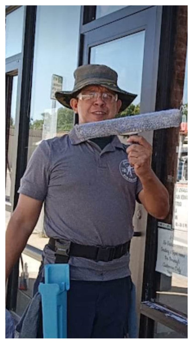 Professional window cleaner holding a t-bar scrubber while wearing safety gear and a sun hat.