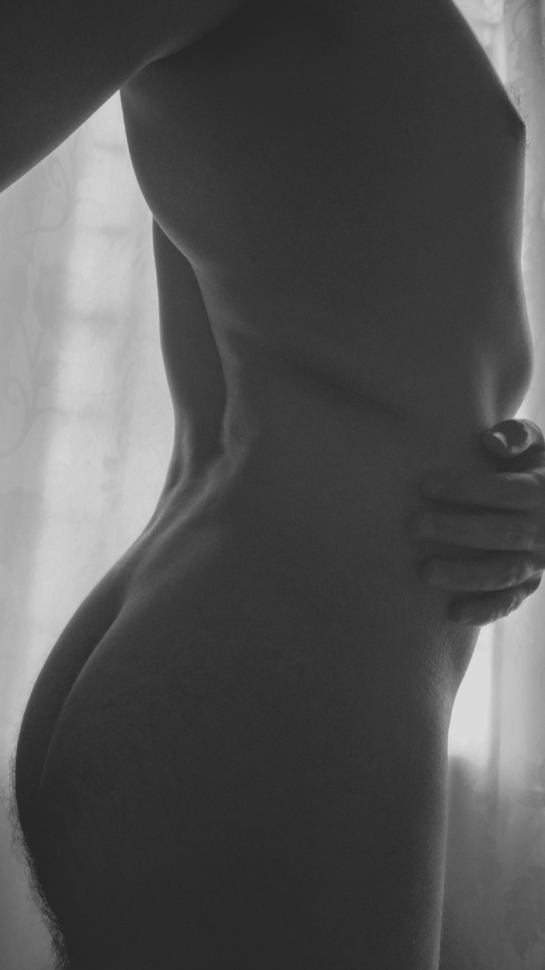 Hombre completamente desnudo de espalda en blanco y negro frente a una ventana.