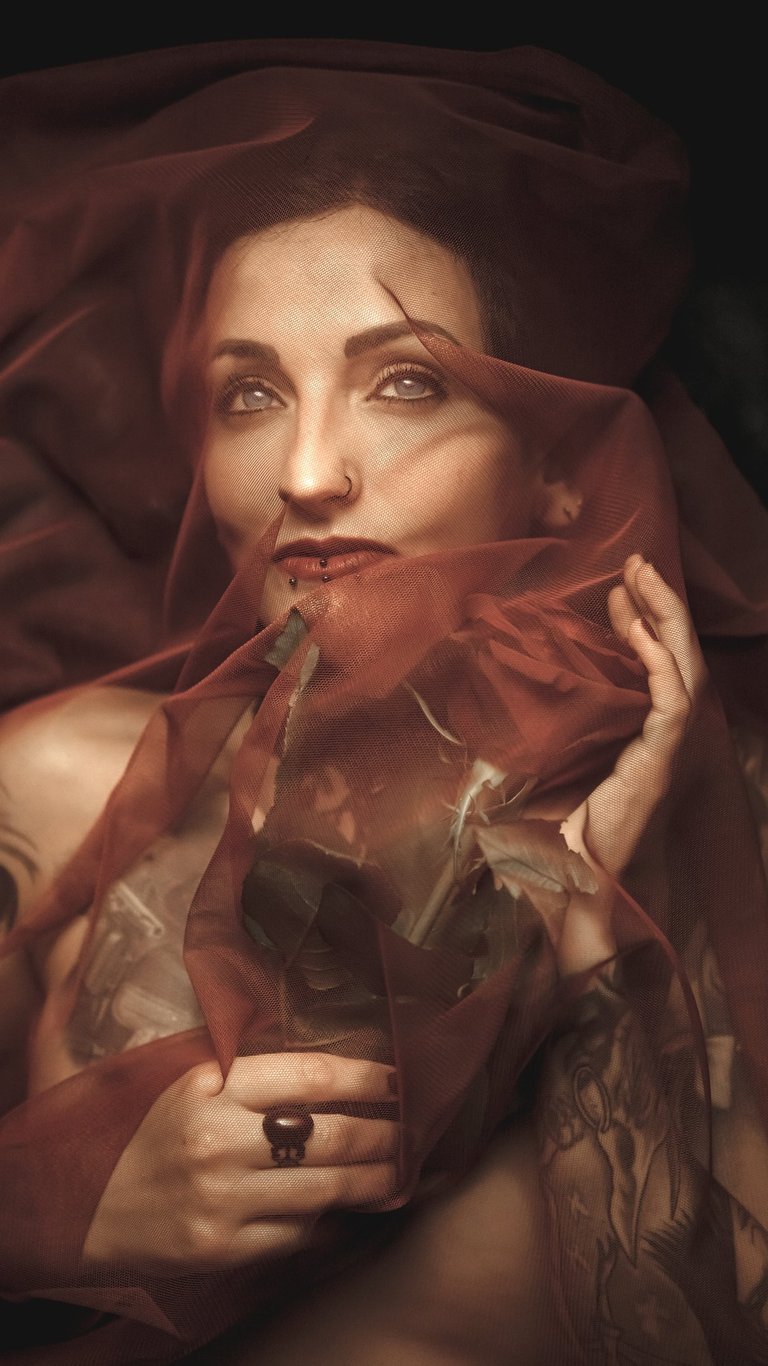 a woman with tattoo in a red dress with a veil on her head holding a red rose