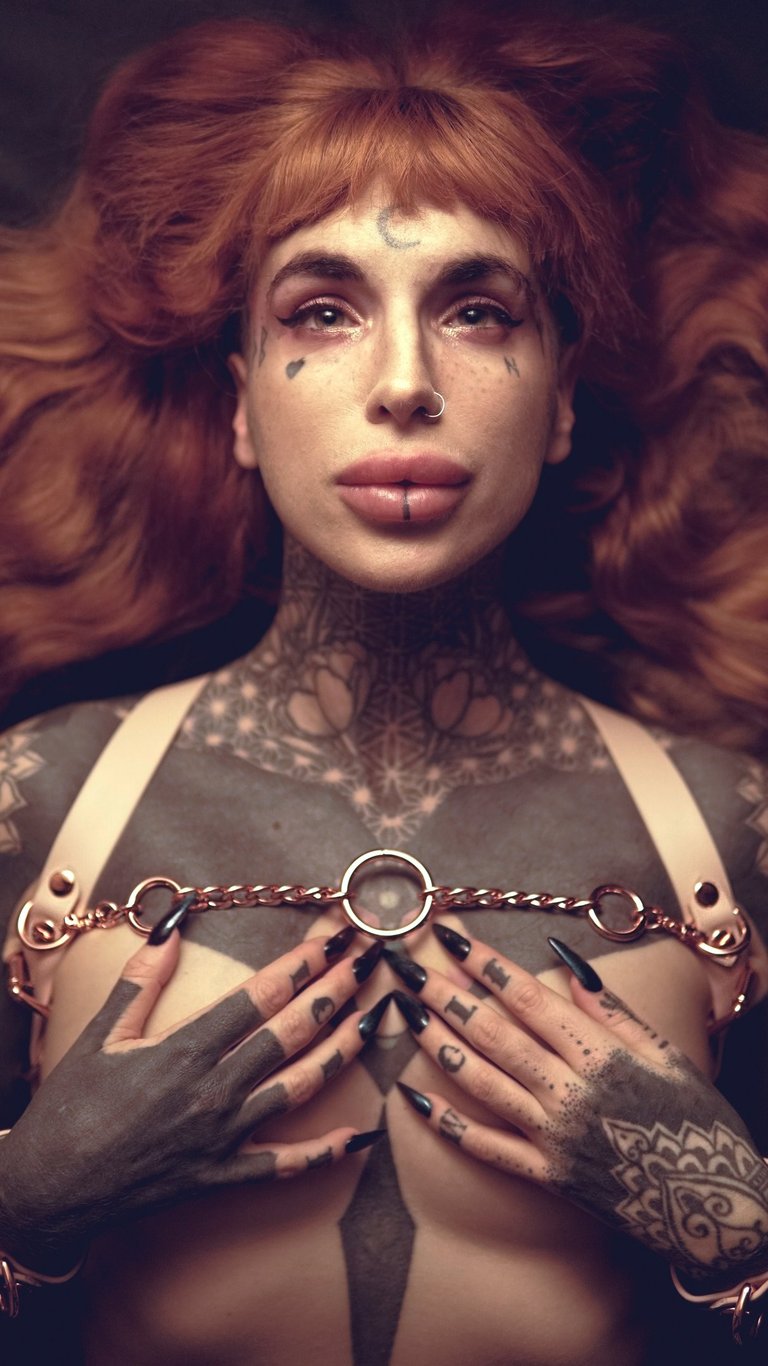 a woman with ginger hair with tattoos on her chest and wearing a harness