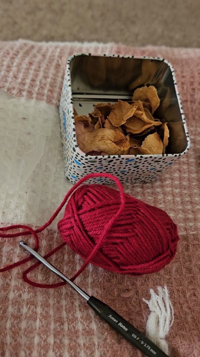 red yarn next to a crochet hook and dried rose petals
