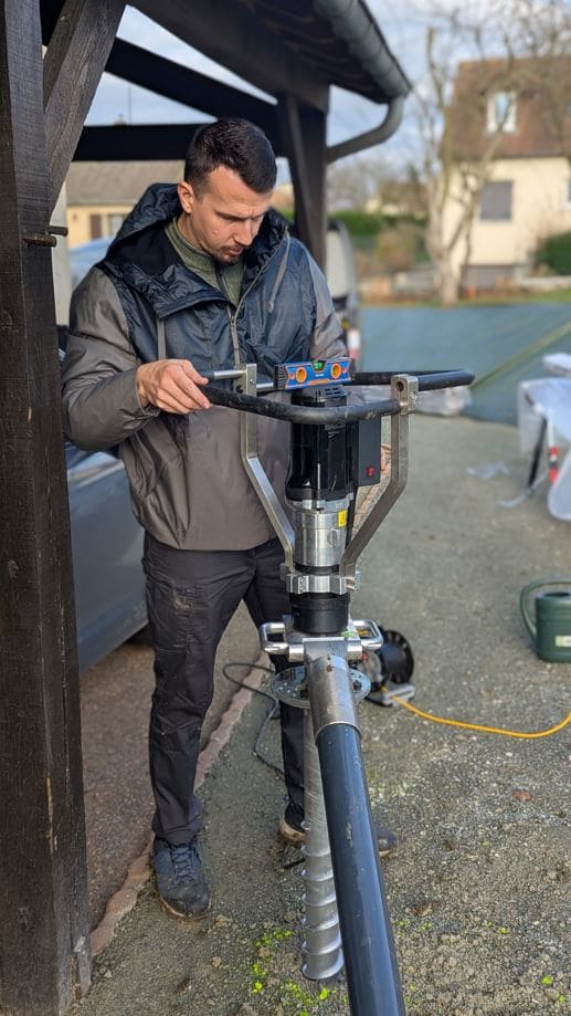 Technicien réglant la verticalité d'une vis de fondation pour un abri