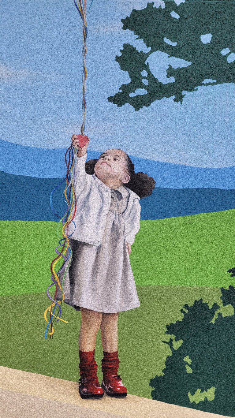 Fresque peinte: une fillette tient une grappe de ballons, debout sur un muret, Jura, Viry (39).