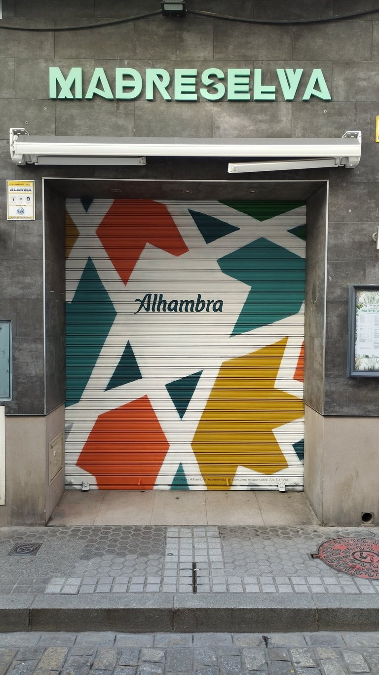 Graffiti corporativo Cervezas Alhambra en cierre metálico de restaurante MadreSelva en Sevilla