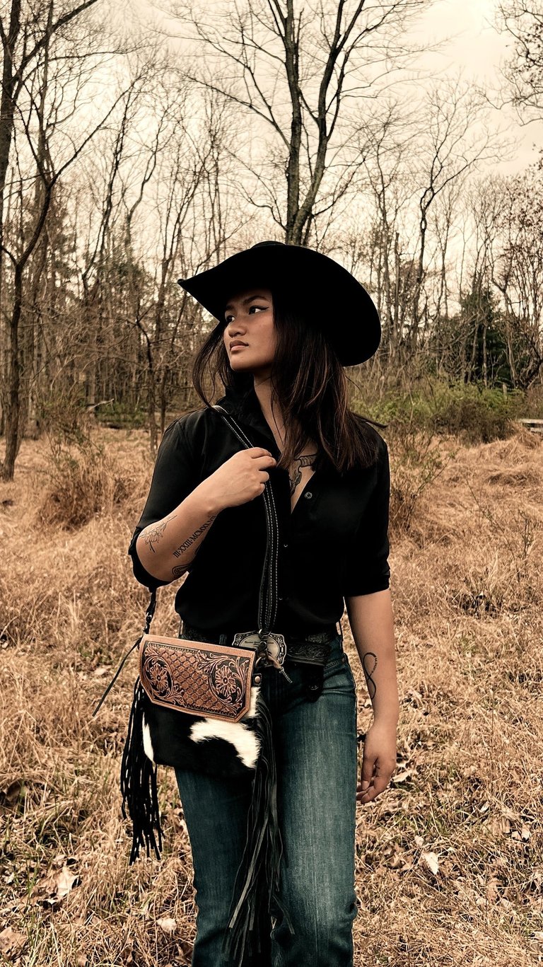 Woman in a black top and black cowboy hat walking in the woods