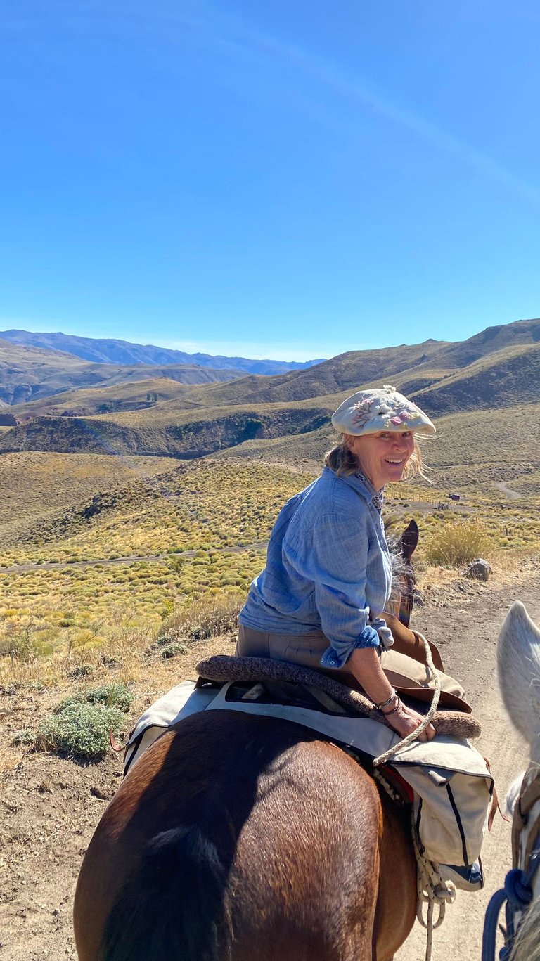 A person on a horse smiling with a mountainous landscape behind them.