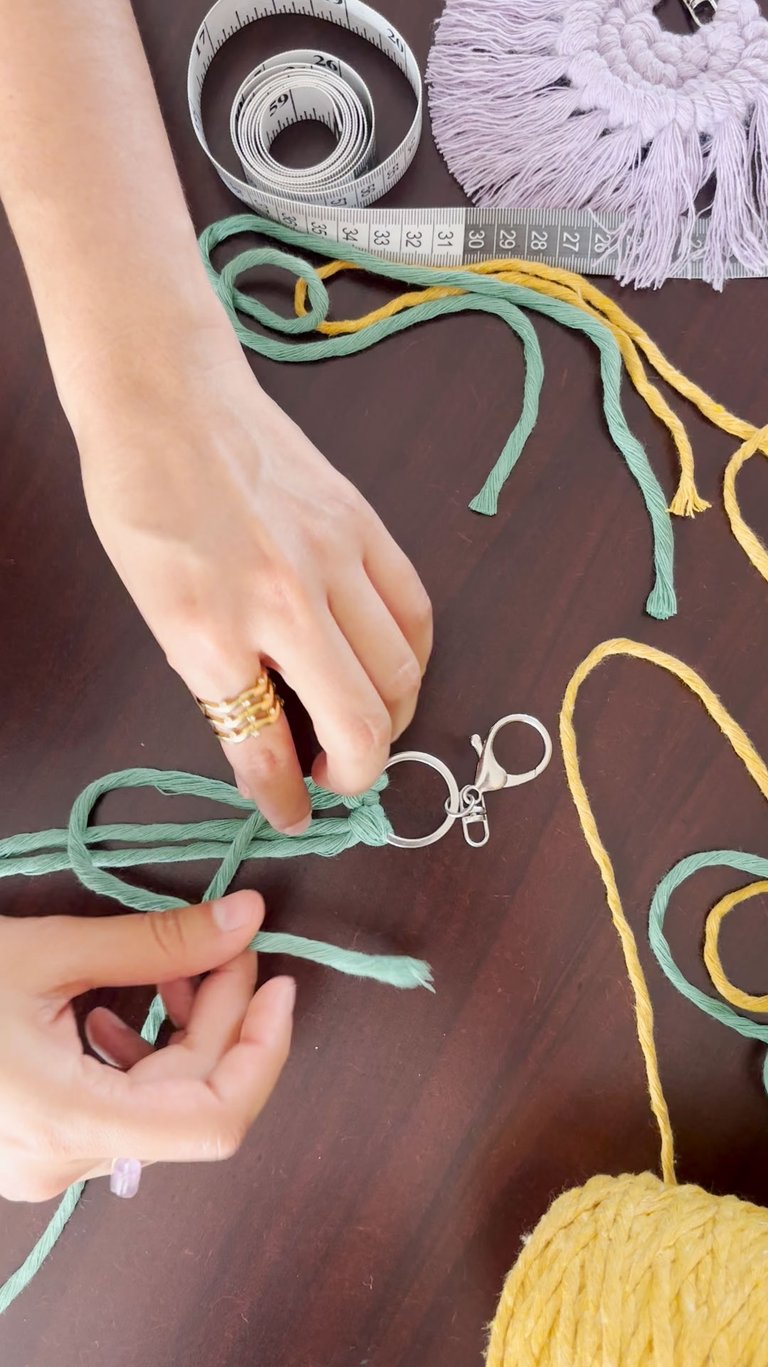 manos tejiendo un llavero de maramé azul y cordones de colores sobre la mesa de trabajo