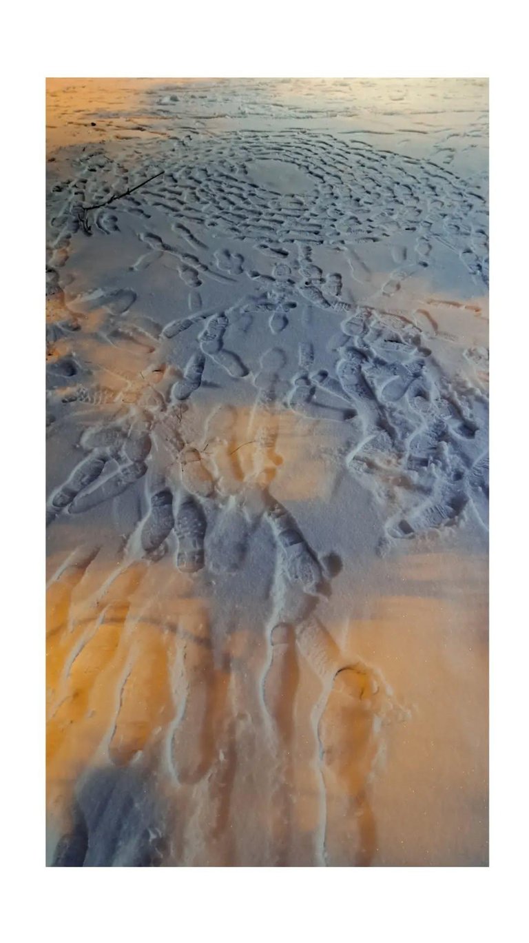 Boot footprints forming circular patterns in fresh snow illuminated by golden sunset light.