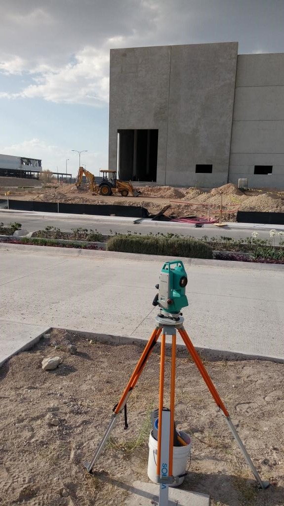 A digital total station on a tripod performing land surveying at a commercial building construction site.