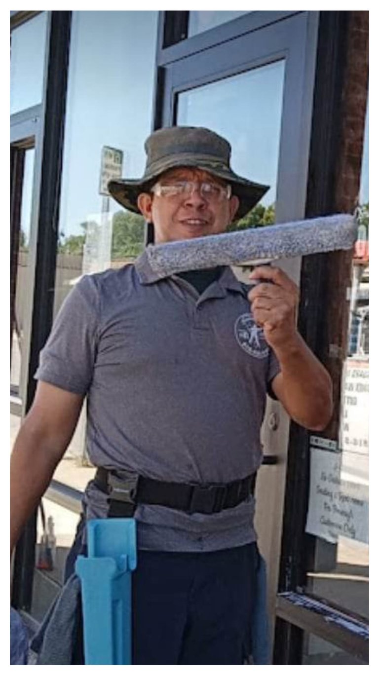Professional window cleaner holding a t-bar scrubber while wearing safety gear and a sun hat.