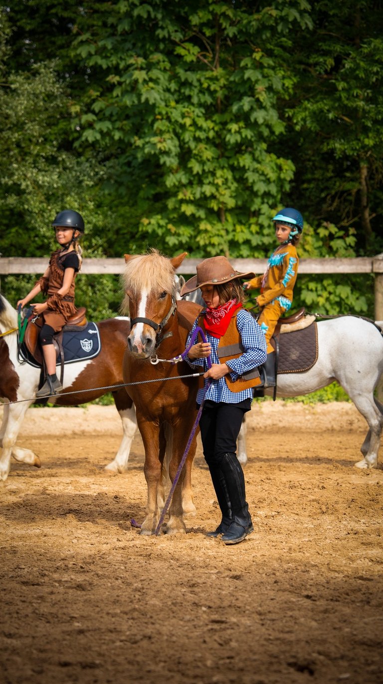 a group of people riding horses in a dirt field and a boy dressed like cowboy