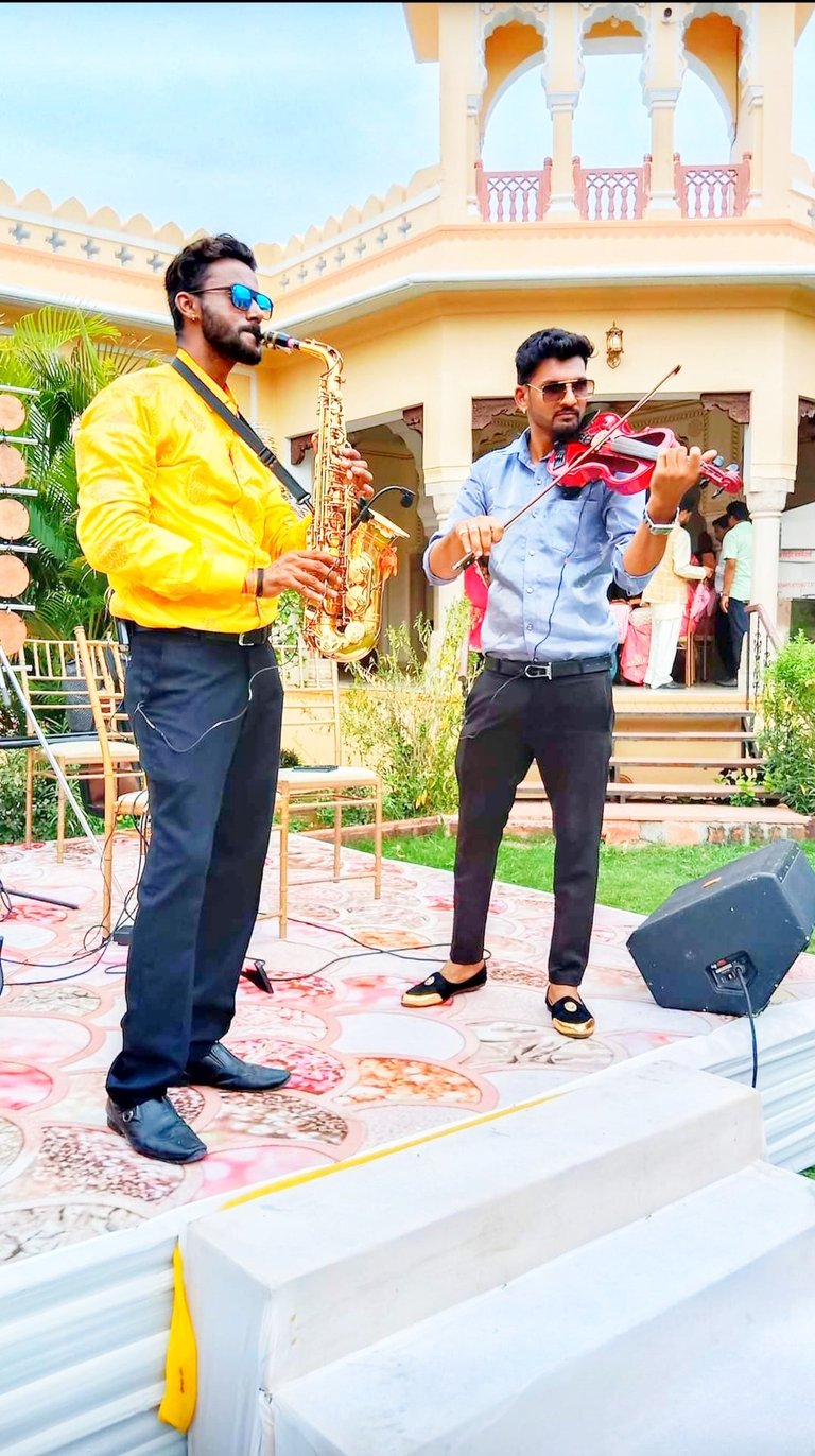 Professional musicians performing with a golden saxophone and red violin at an outdoor event.