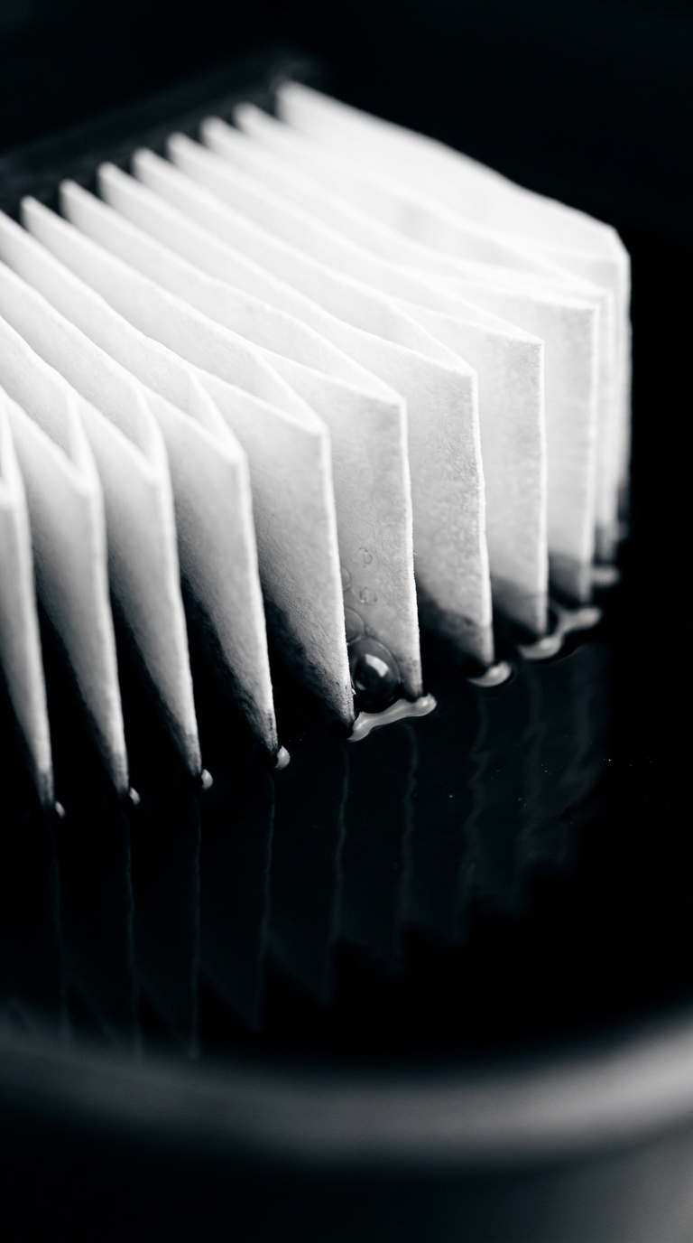 A white pleated air filter partially submerged in dark water, showing moisture absorption and filtration detail.
