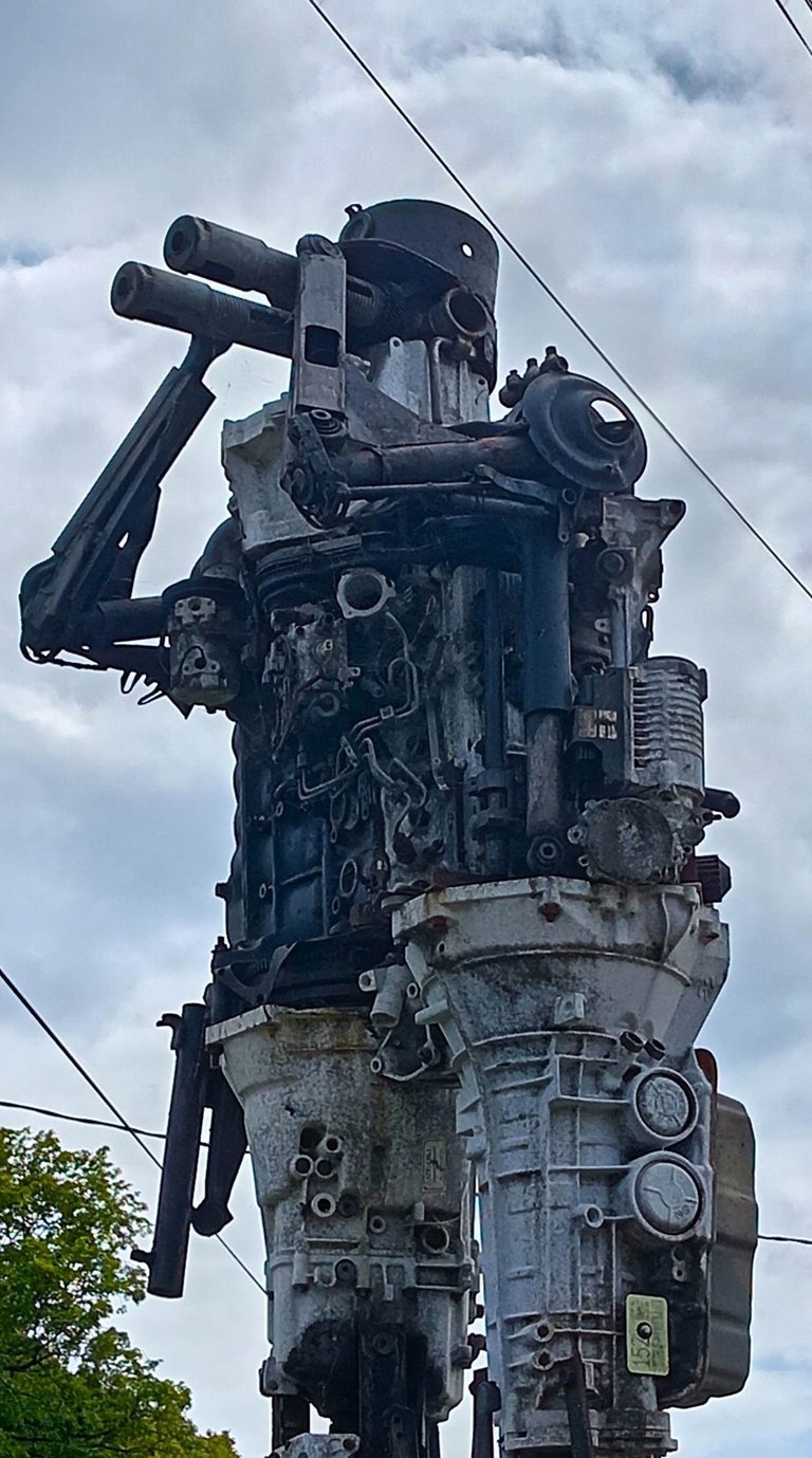 Tall steampunk robot sculpture made from recycled car engines and mechanical scrap metal parts.