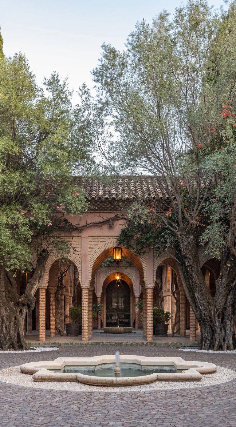 Arched brick courtyard framed by ancient olive trees and central fountain