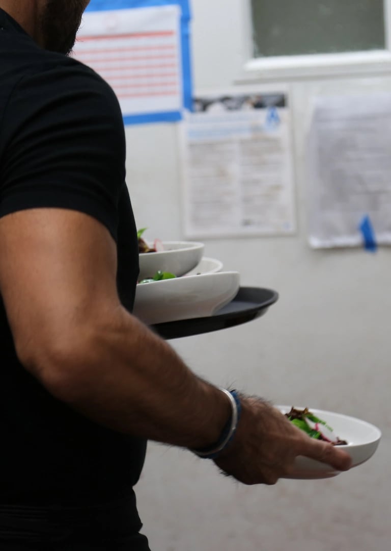 Close-up of a server dressed in black, carrying several plates with both hands.