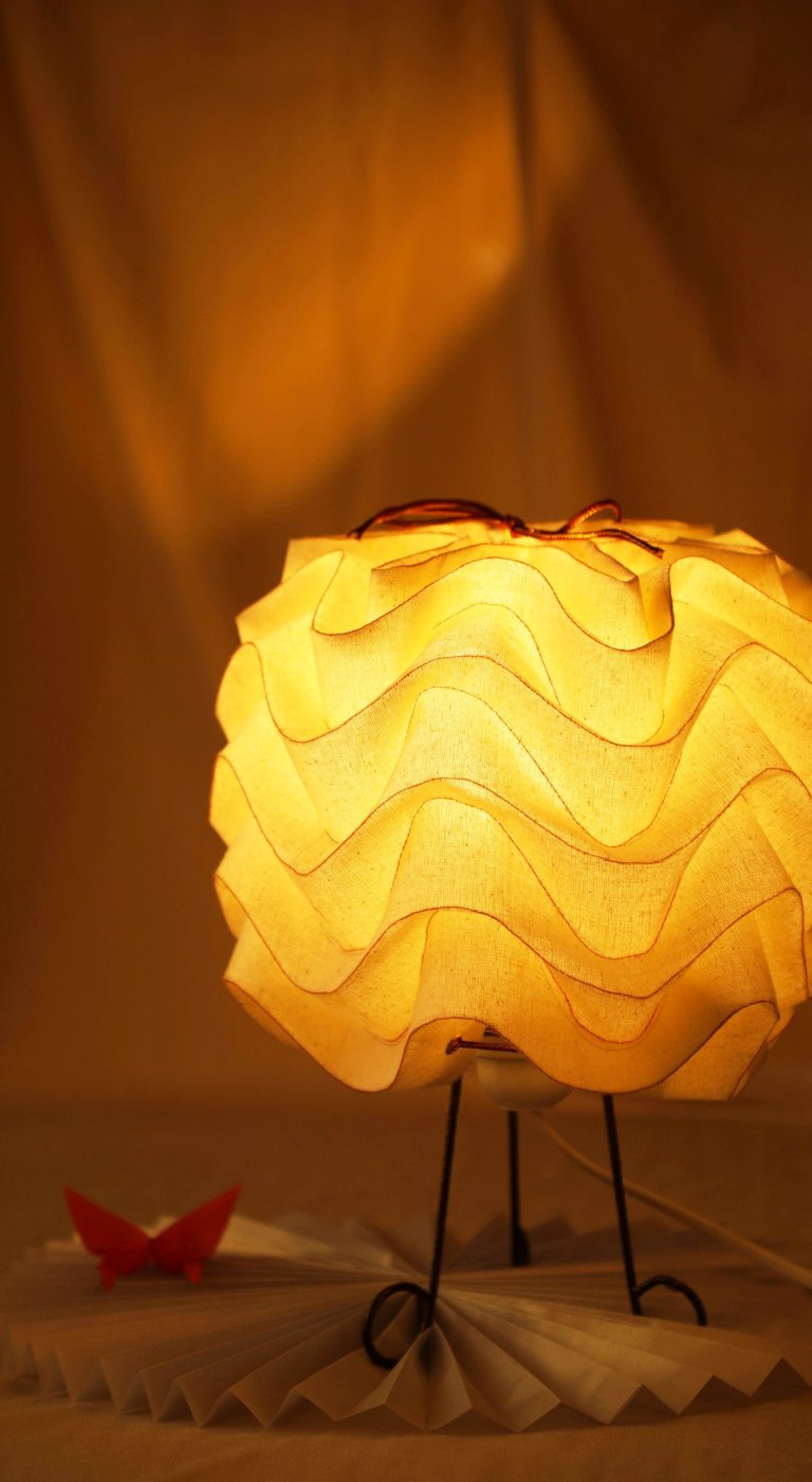 Warm yellow textured fabric table lamp glowing in a dark room with a red origami butterfly.