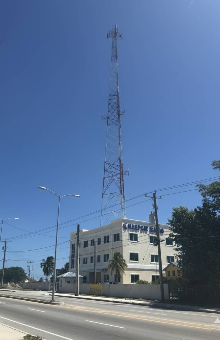 Tall communications tower standing behind the Keepsie Radio building under a clear blue sky.