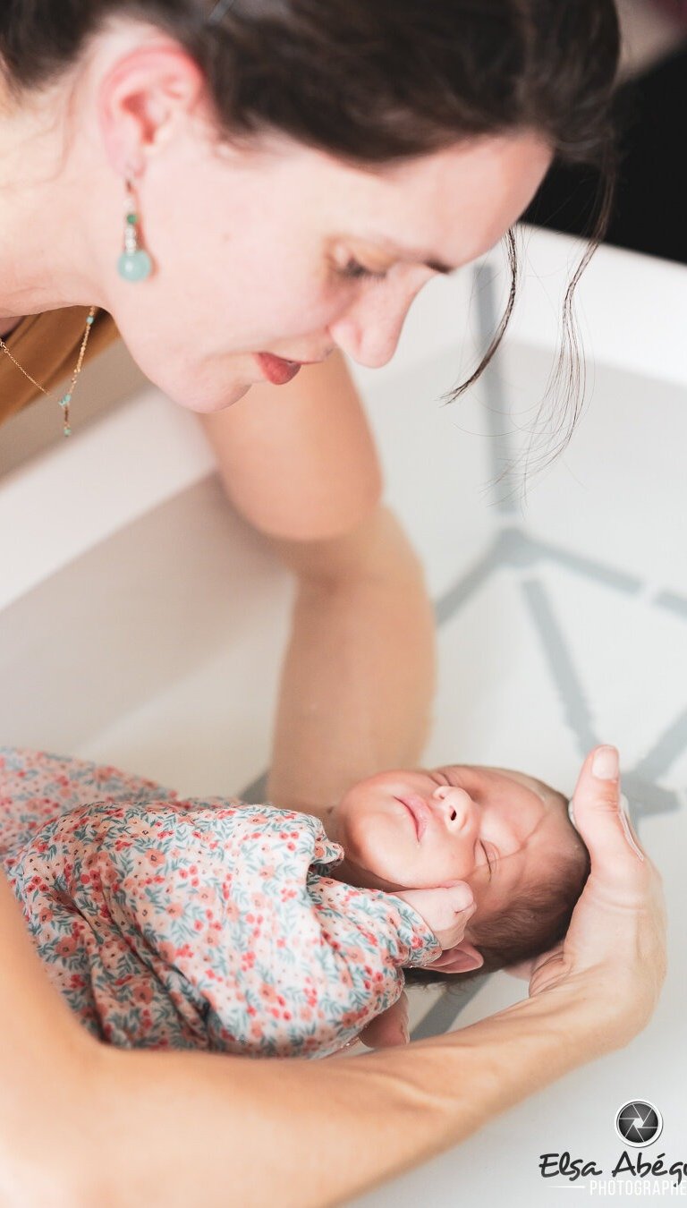 Bébé emmaillotté dans une couverture, dans les bras d'Audrey pendant le Bain des Merveilles