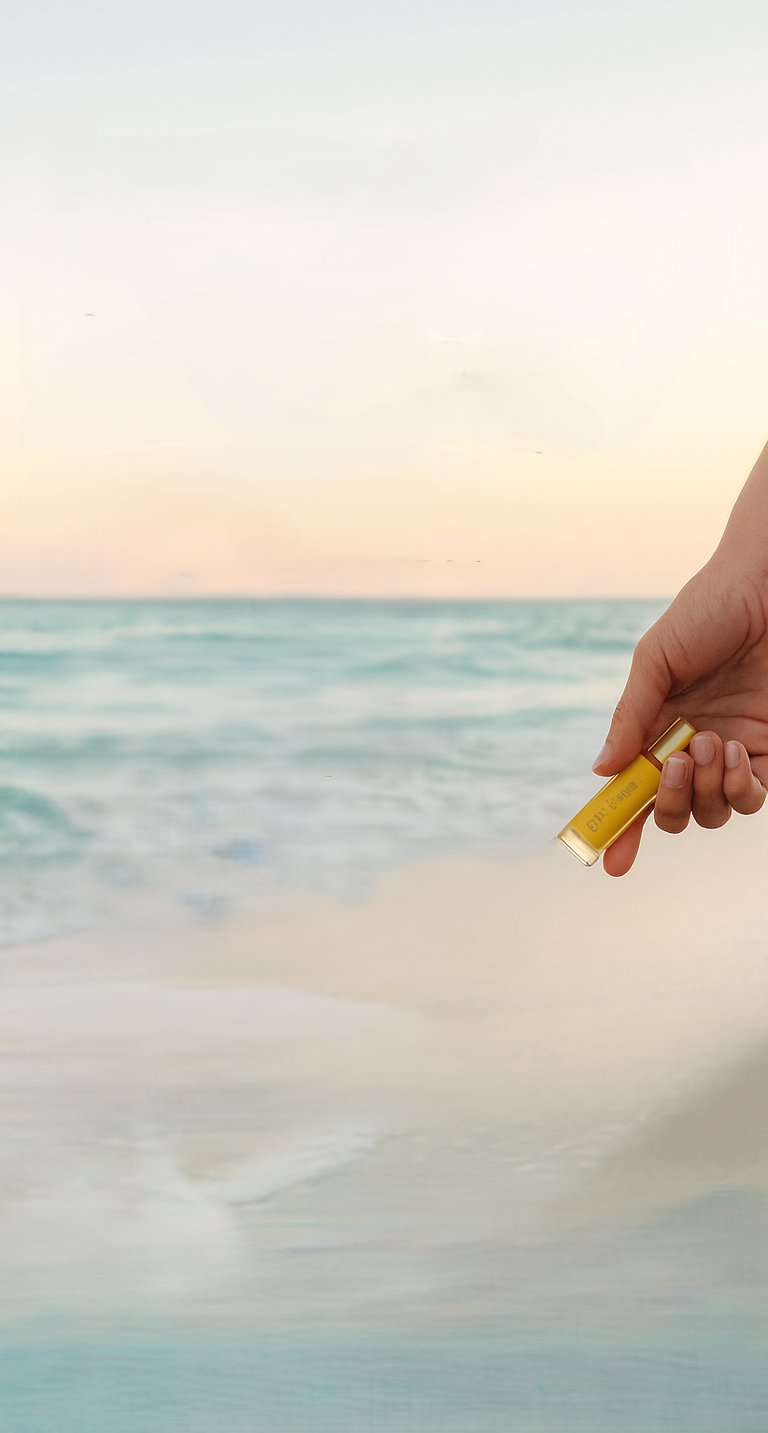 image of hand holding an essential oil bottle beachside