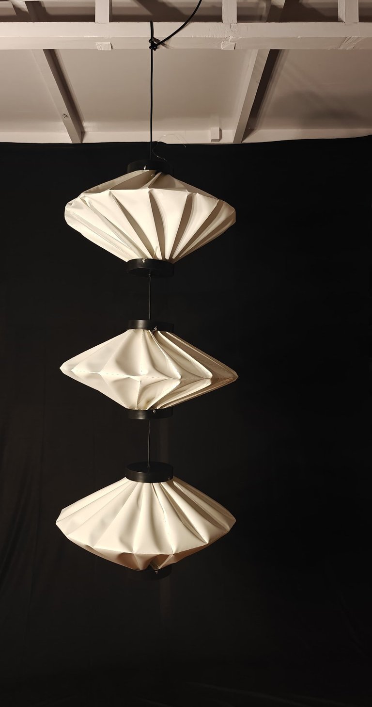 Dumpling shaped modern pleated paper light hanging against a black backdrop.