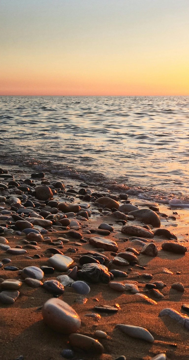sand and pebble beach with sun setting over the calm sea