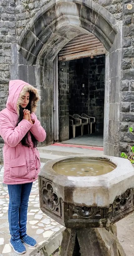 Visitor tossing a coin into the wishing well at St. John in the Wilderness Church, McLeod Ganj.