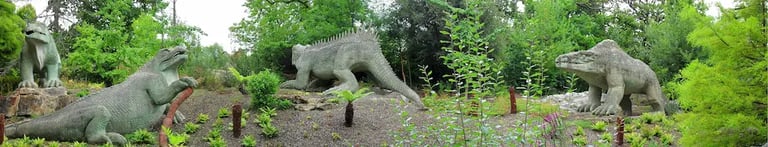 Panoramic view of the Victorian Crystal Palace Dinosaurs sculptures in a lush park setting.
