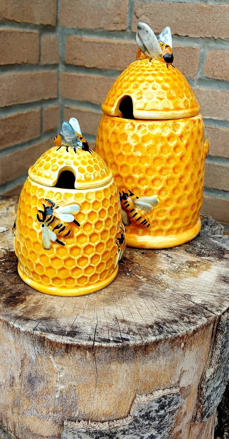 Two yellow ceramic honeycomb beehive honey pots decorated with bees on a rustic tree stump.