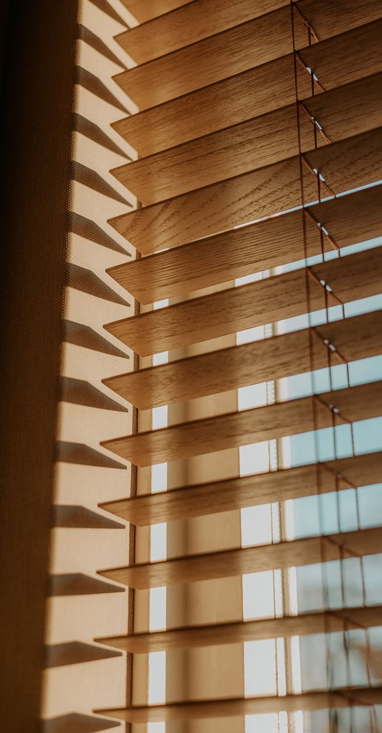 Natural wood horizontal window blinds with sunlight filtering through for home decor.