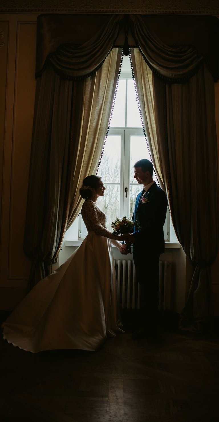 vestuvių fotosesija dvaro viduje. a bride and groom standing in front of a window
