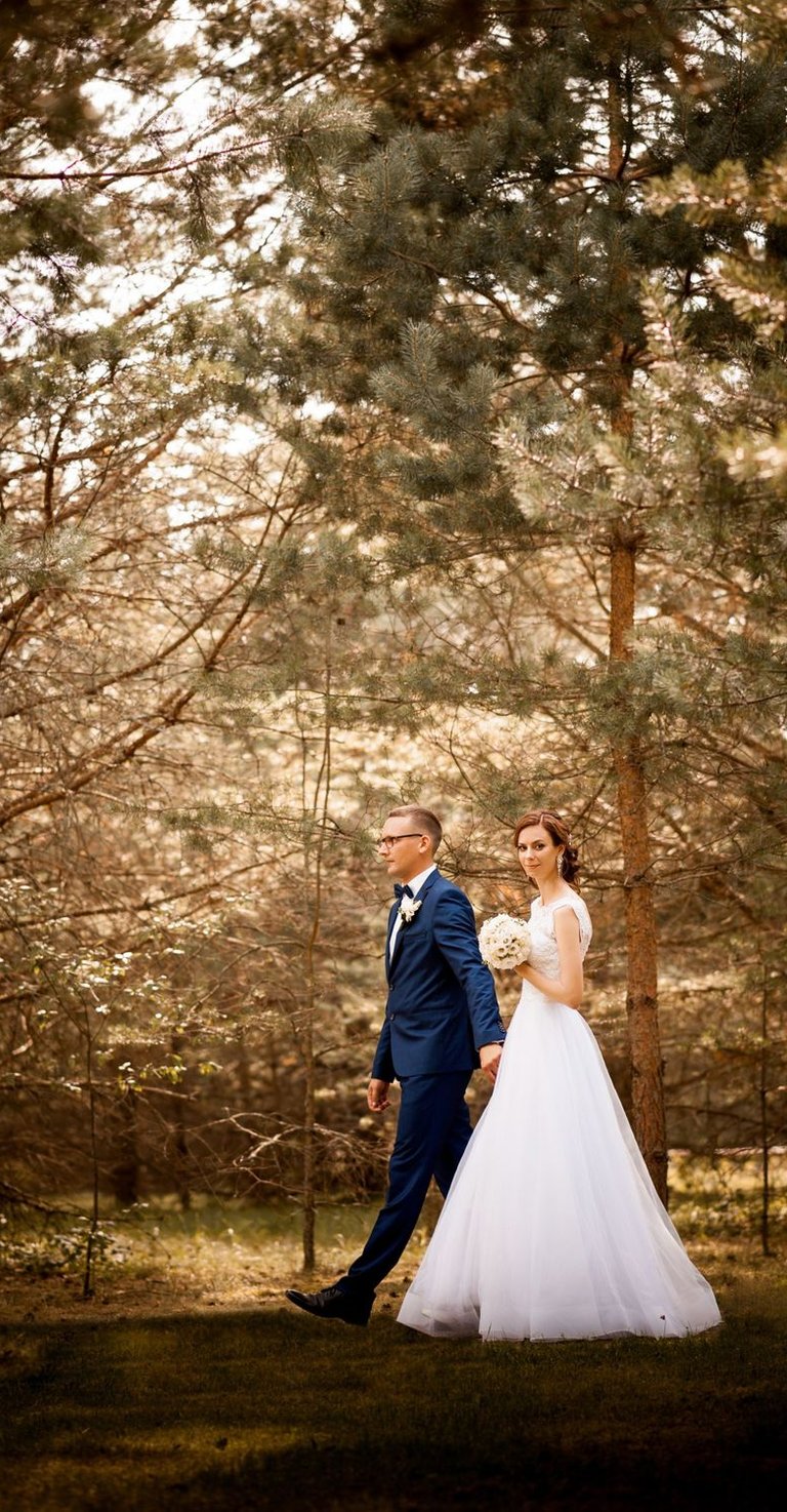 a bride and groom walking through a wooded area