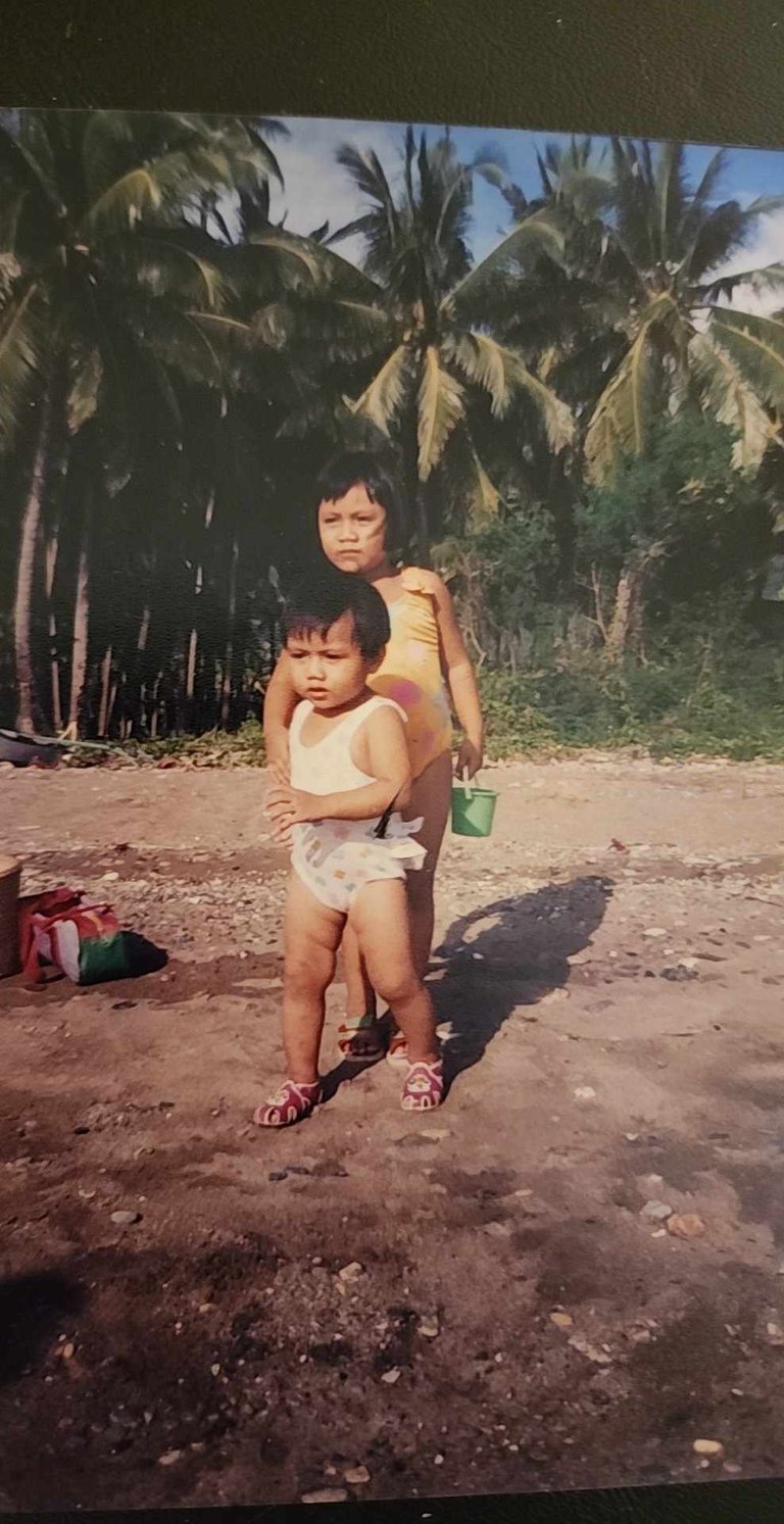 My sister and I on the beach, tropical foliage in the background.