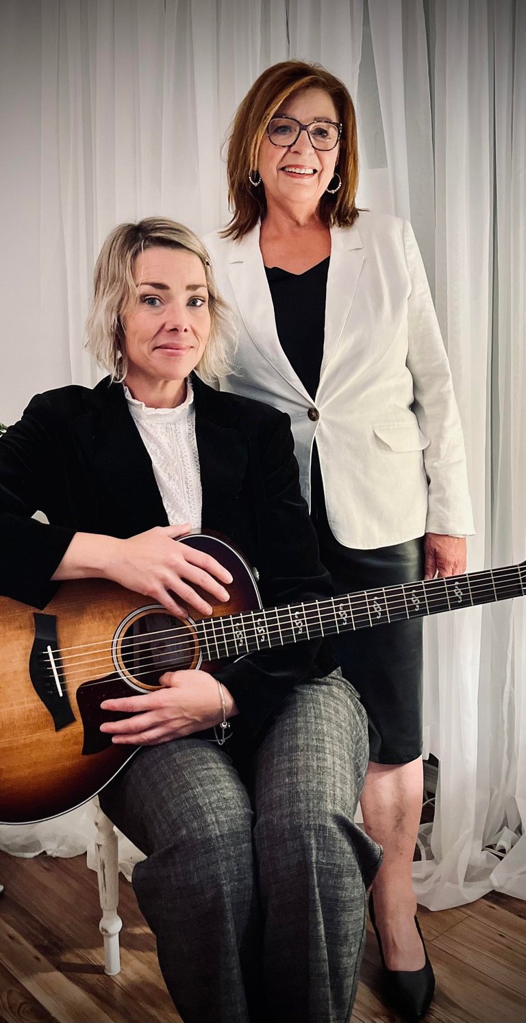 Colette et Caroline Lupien posent, l’une assise avec une guitare, l’autre debout, souriante. 