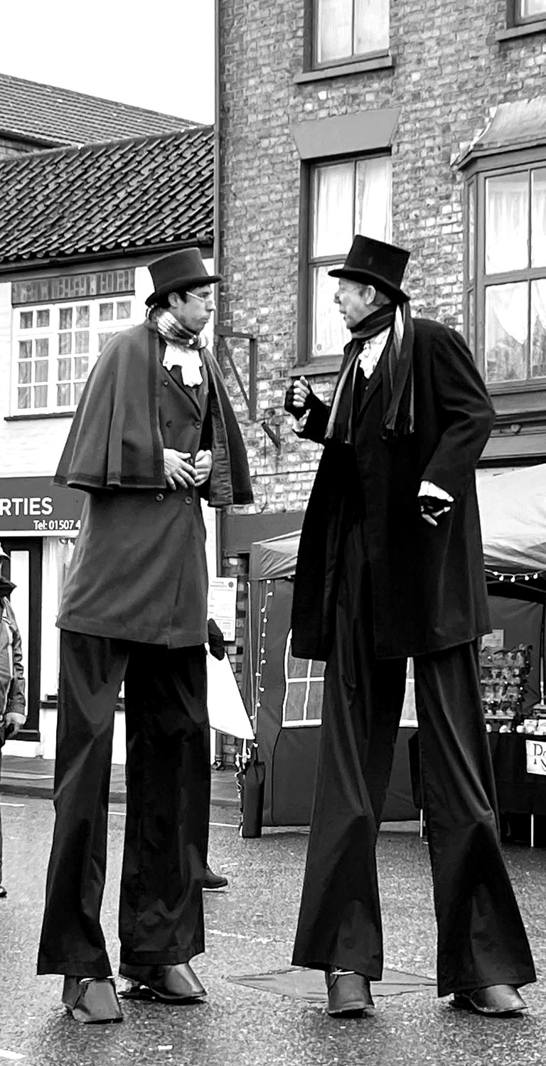 Two street performers on high stilts wearing Victorian costumes and top hats at a christmas event