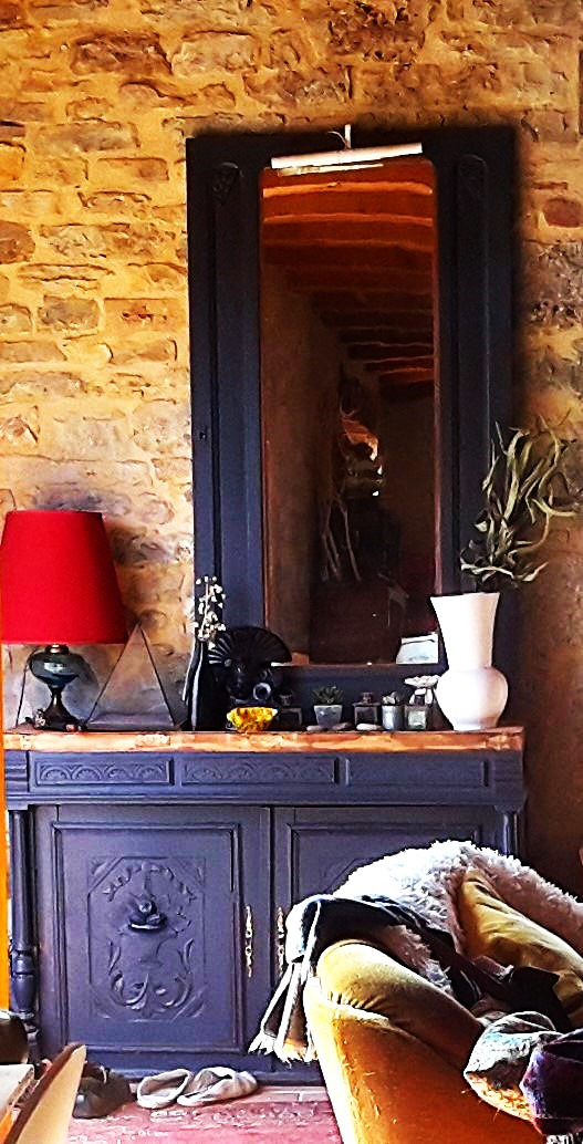 Rustic stone wall featuring a black vintage sideboard and matching framed mirror with elegant home decor.