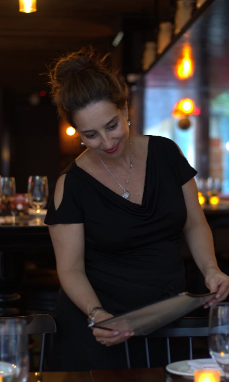 Smiling woman dressed in black, holding a menu in a restaurant setting