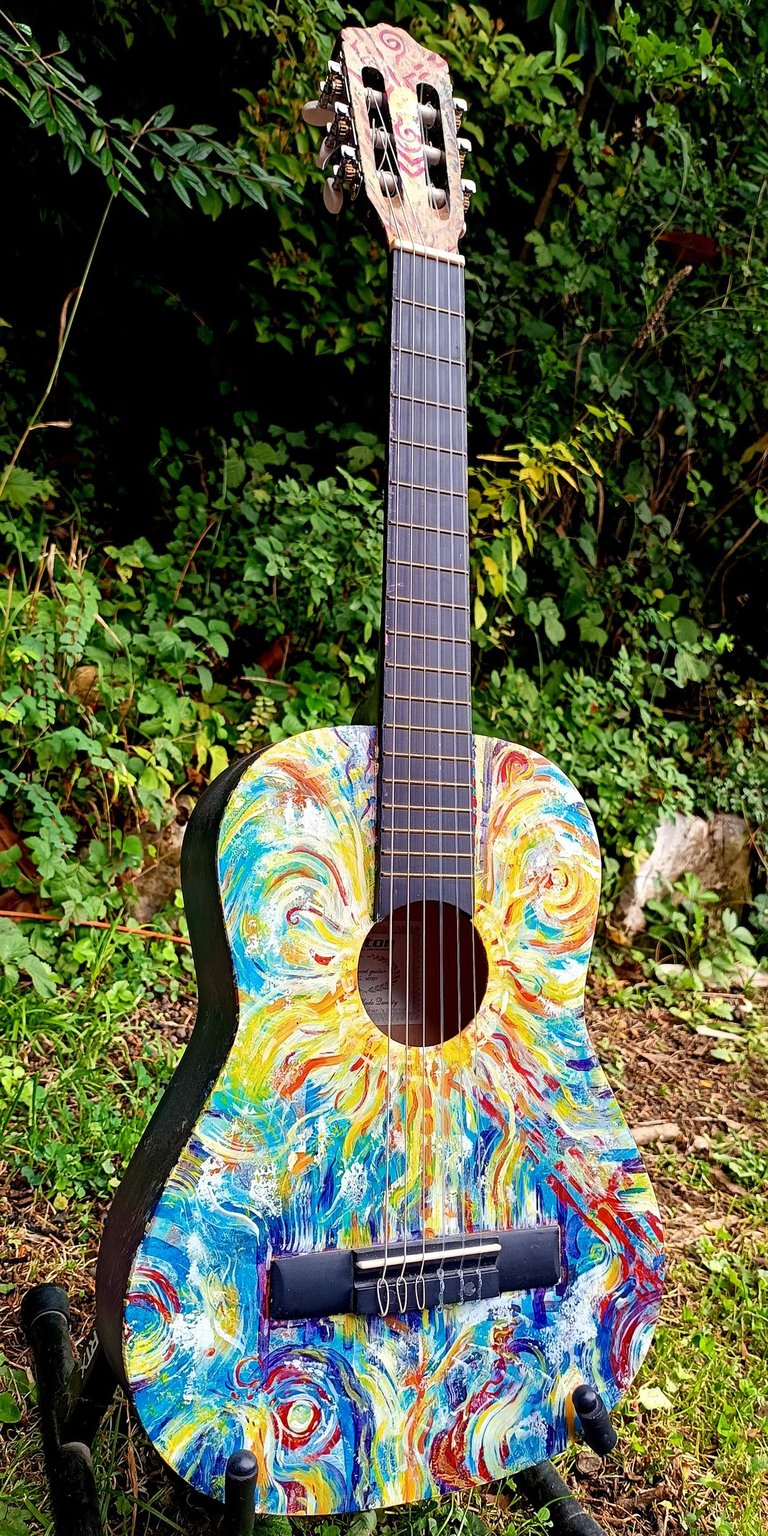 peinture sur guitare aux couleurs vives, avec un soleil autour de la rosace et des formes abstraites