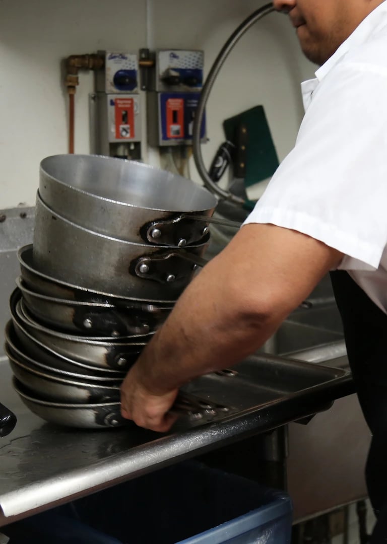 Close-up of a person stacking clean metal pots on a kitchen sink in a professional kitchen setting.