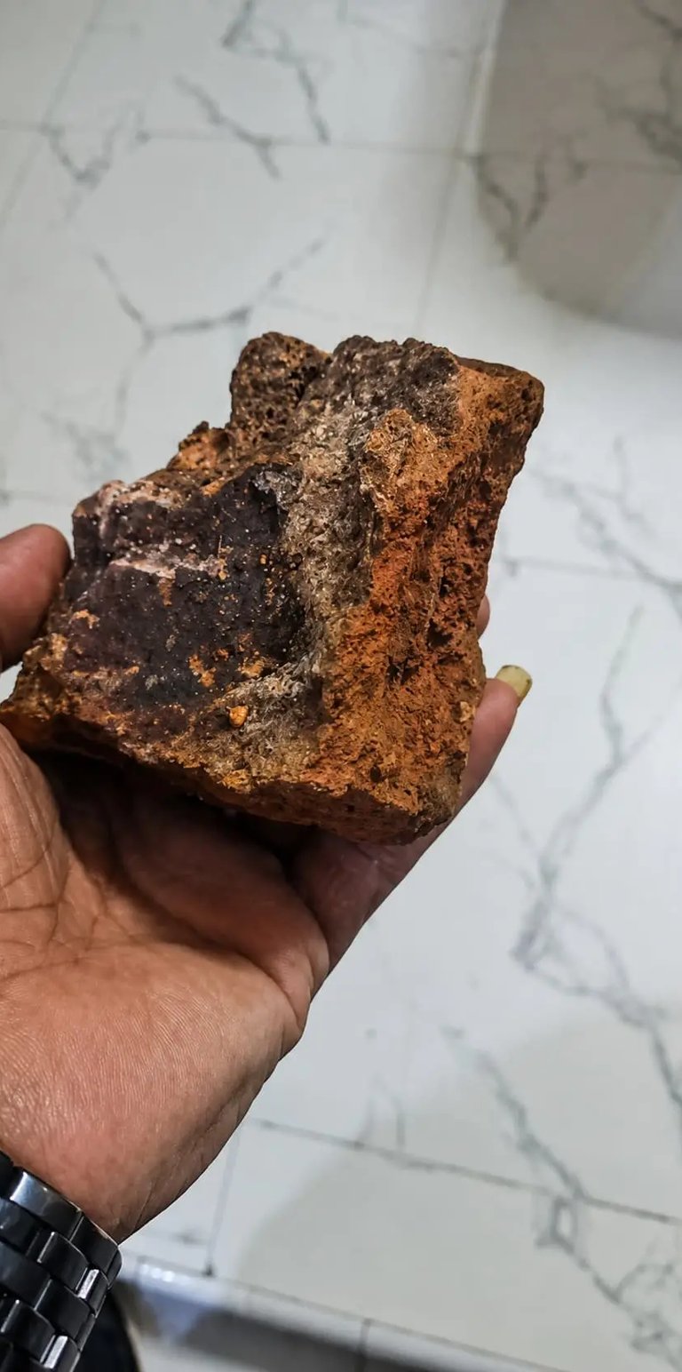 A hand holding a rough iron ore rock specimen with visible red hematite and dark magnetite minerals.