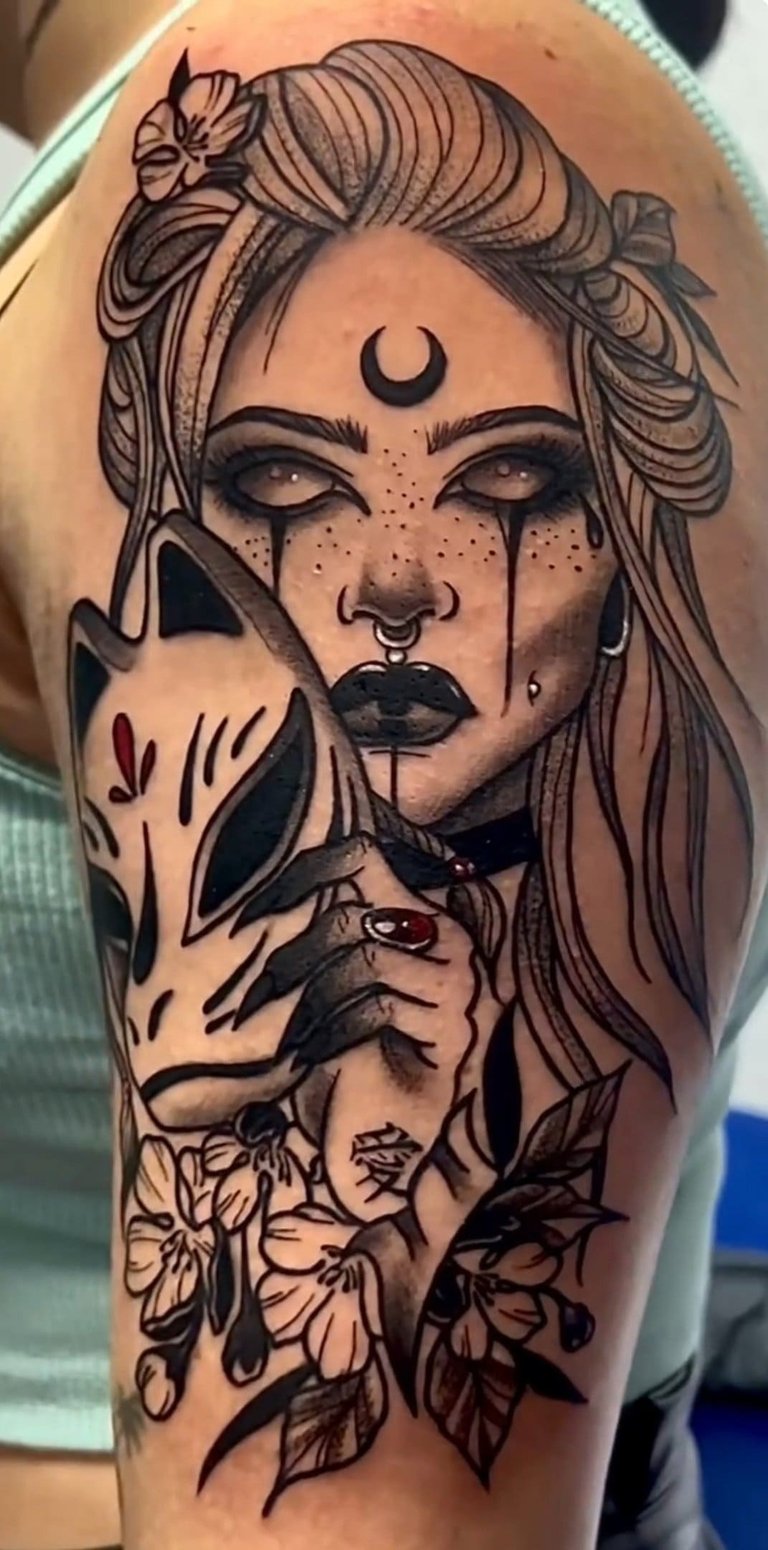Detailed black and grey ink tattoo on shoulder featuring a gothic woman with a crescent moon and kitsune mask.